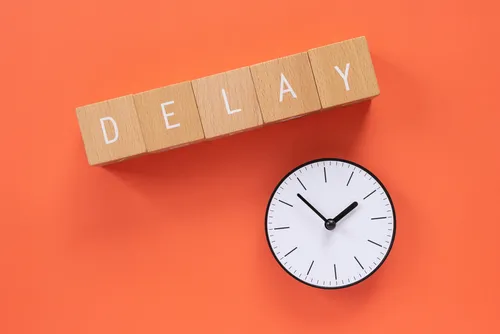 Wooden blocks spelling delay beside a clock