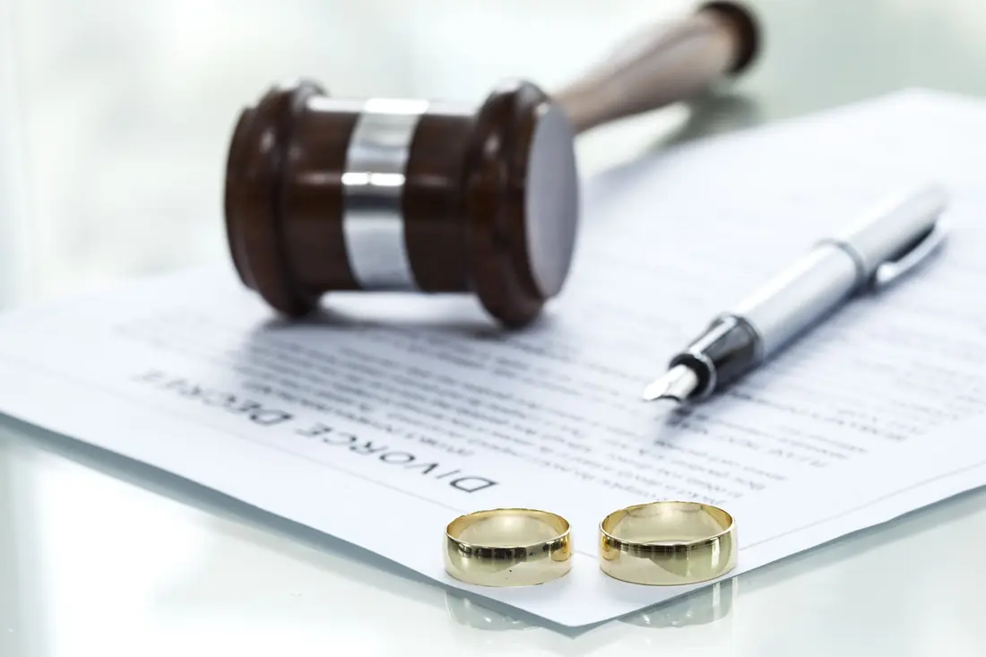 Two wedding rings on divorce papers beside a gavel and pen