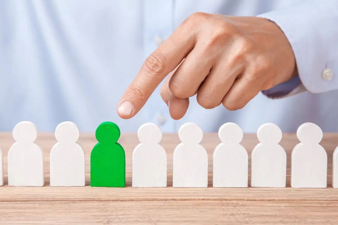 Hand pointing to one green figure in a row of white figures