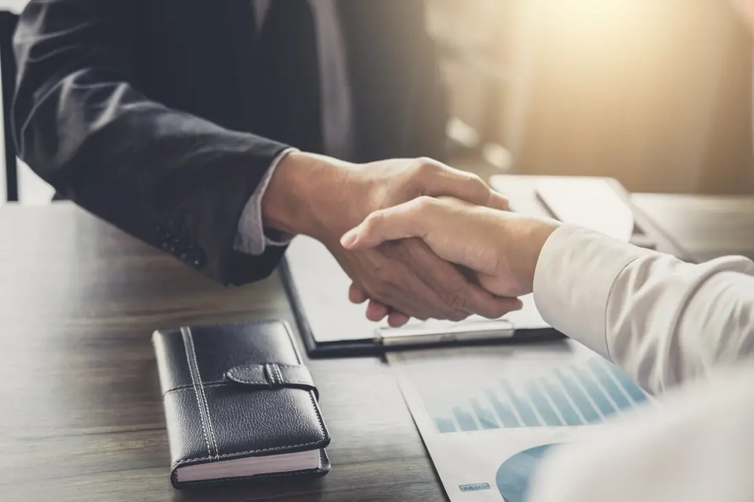 Two people shaking hands over a desk