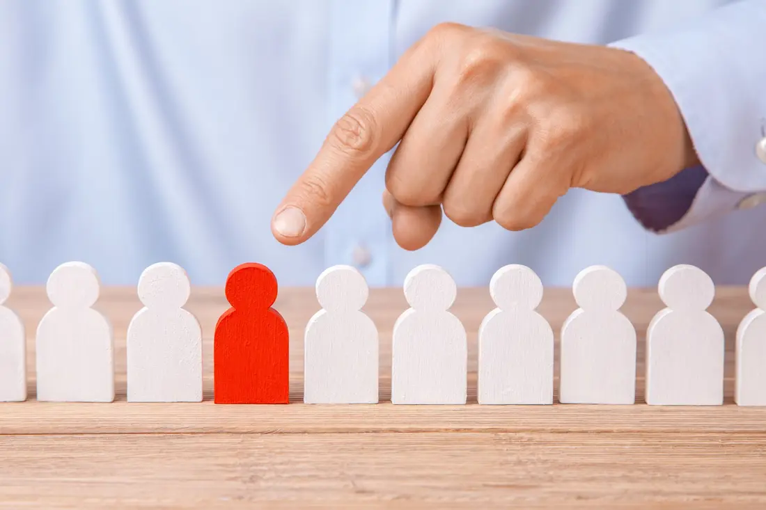 Hand pointing to one red figure in a row of white figures