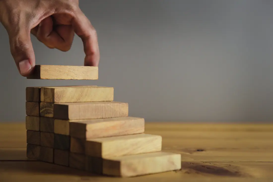 Hand placing a wooden block on a set of steps